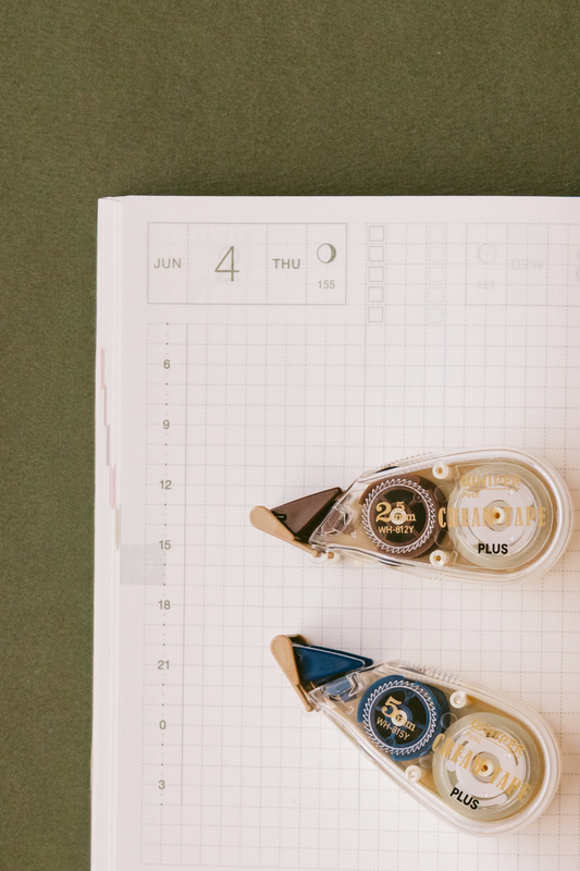 Two Whisper Chara Tape Plus dispensers—one brown for 25mm width (10m) and one blue for 50mm width (9m)—with built-in cutters, arranged on graph paper.
