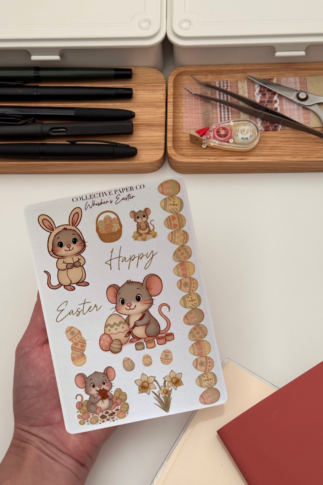 Sheet of Easter-themed stickers with cartoon mice and eggs held by a hand, with stationery items in the background.