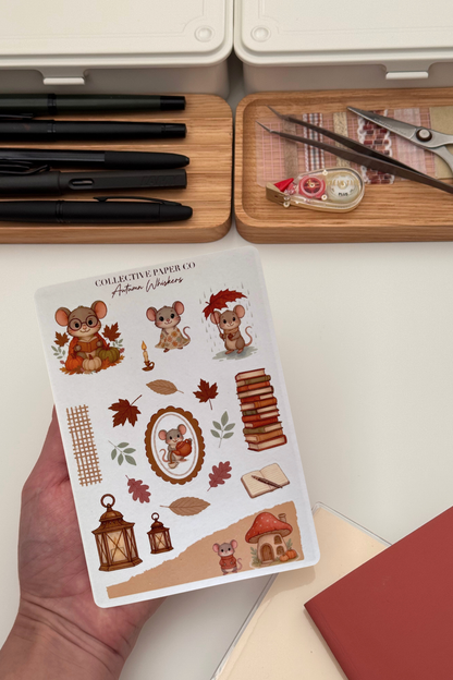 Sheet of autumn-themed stickers held by a hand with stationery items in the background.