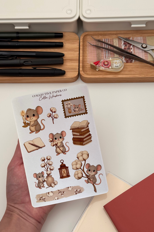 Sheet of mouse-themed stickers held by a hand with stationery items in the background.