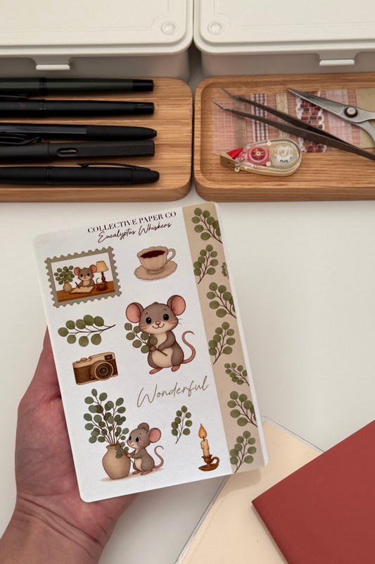 Sheet of decorative stickers with mouse illustrations held by a hand, with stationery items in the background.