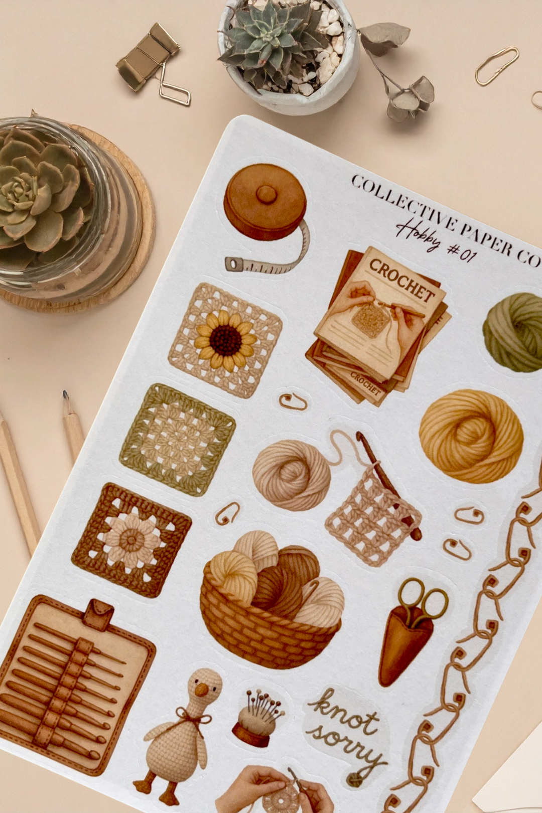 Sticker sheet with crochet-themed designs on a beige surface with plants and stationery items.