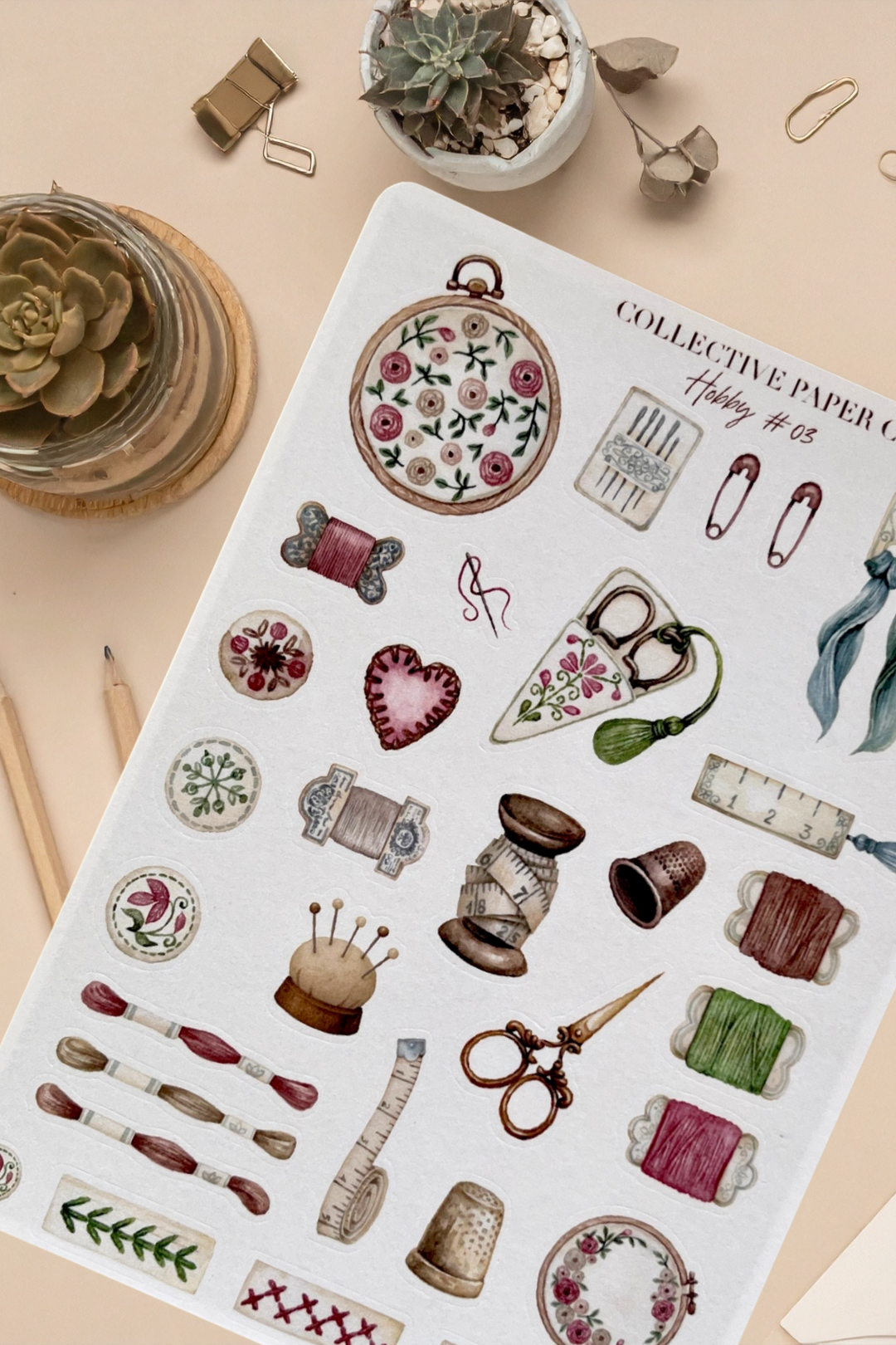 Sheet of decorative stickers with sewing-themed designs on a beige surface.