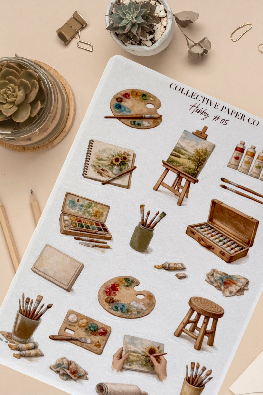 Sticker sheet with artistic illustrations on a beige surface with stationery items.