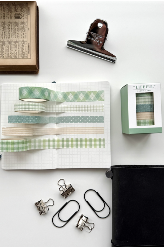 Lifefull green gingham masking tapes on grid notebook, clips, black journal, book, red clip in flat lay.