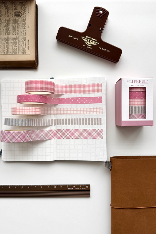 Lifeful pink gingham masking tapes on grid notebook, ruler, clips, brown journal, book, red clip in flat lay.