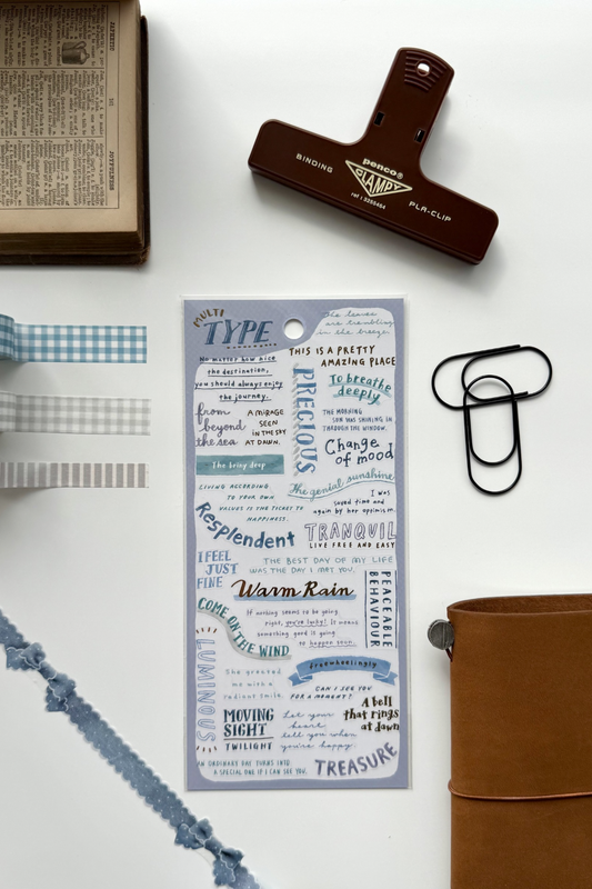 "Type Club" blue inspirational quote washi tape sheet with checkered edges, red binder clip, black clips, book, leather journal in flat lay.
