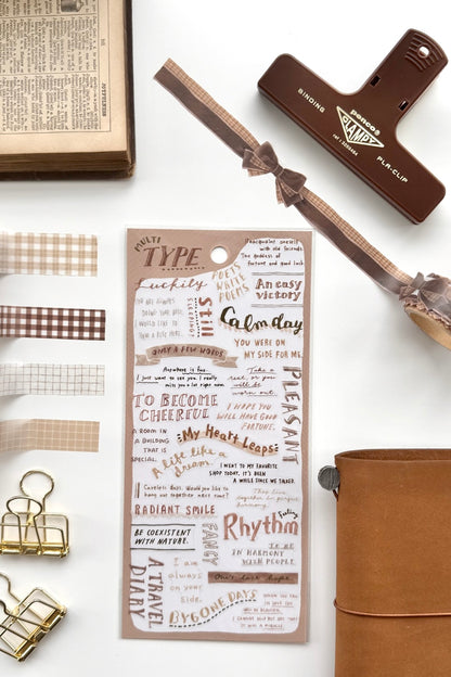 "Type Club" brown inspirational quote washi tape sheet with checkered edges, red binder clip, gold clips, book, leather journal in flat lay.