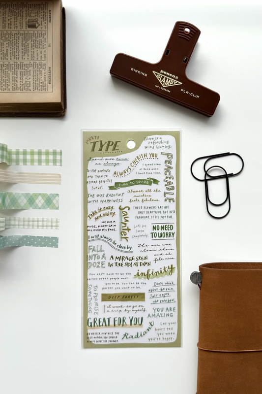 "Type" green washi tape sheet with quotes like "Great for You," "Infinity," and matching checkered tapes, red clip, book, leather journal in flat lay.

