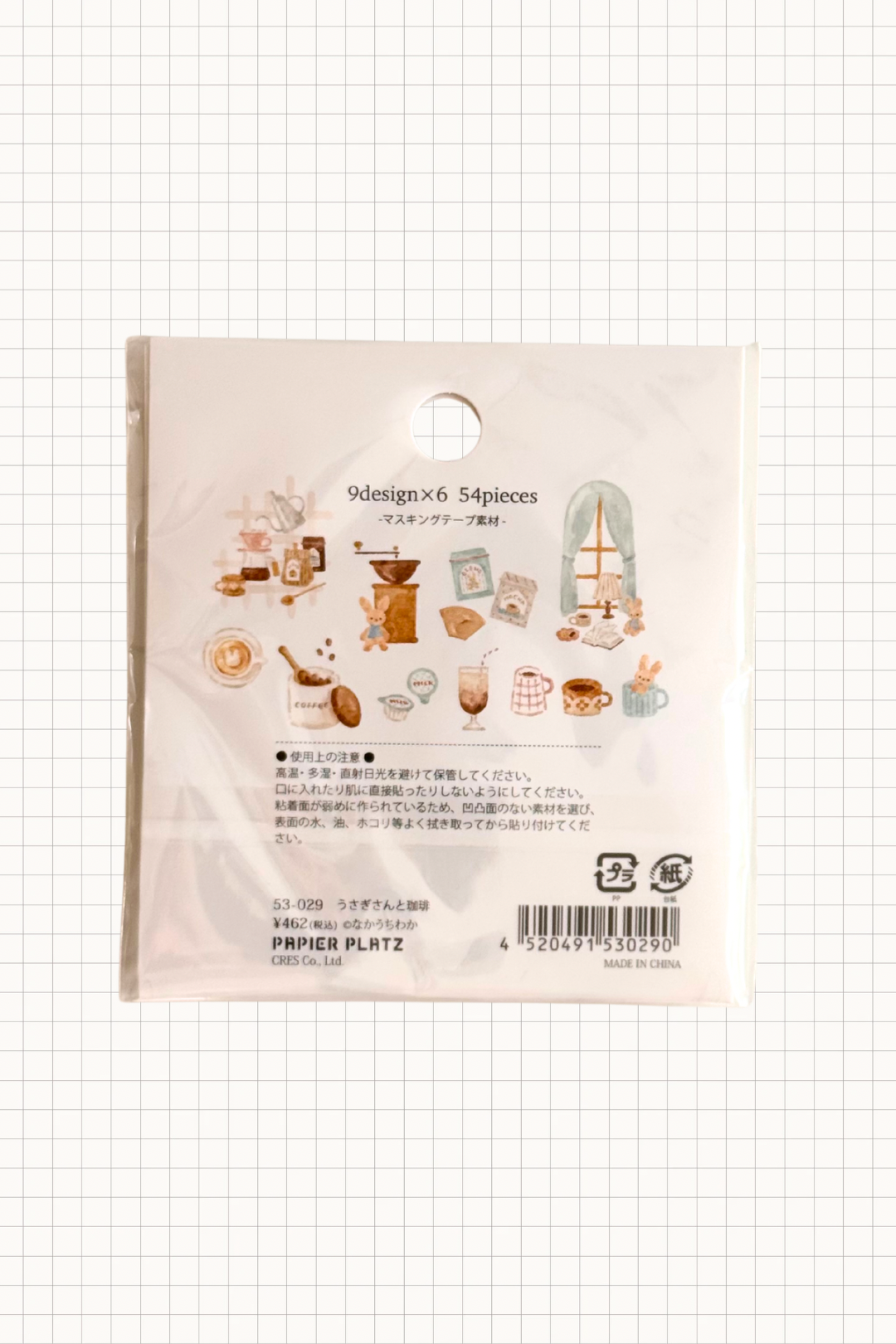 Papier Platz Flake Seal stickers in a soft pink packet, featuring hand-drawn milky drinks, cakes and cosy window scenes with books and lamps on a pale background, shown on grid paper