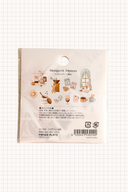 Papier Platz Flake Seal stickers in a soft pink packet, featuring hand-drawn milky drinks, cakes and cosy window scenes with books and lamps on a pale background, shown on grid paper