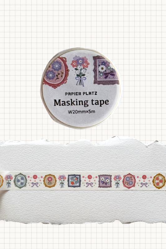 Papier Platz masking tape roll with repeating frames and tiny flower bouquets in purple, pink and gold on cream tape, shown on grid background with a swatch of the 20 mm wide 5 m tape unrolled