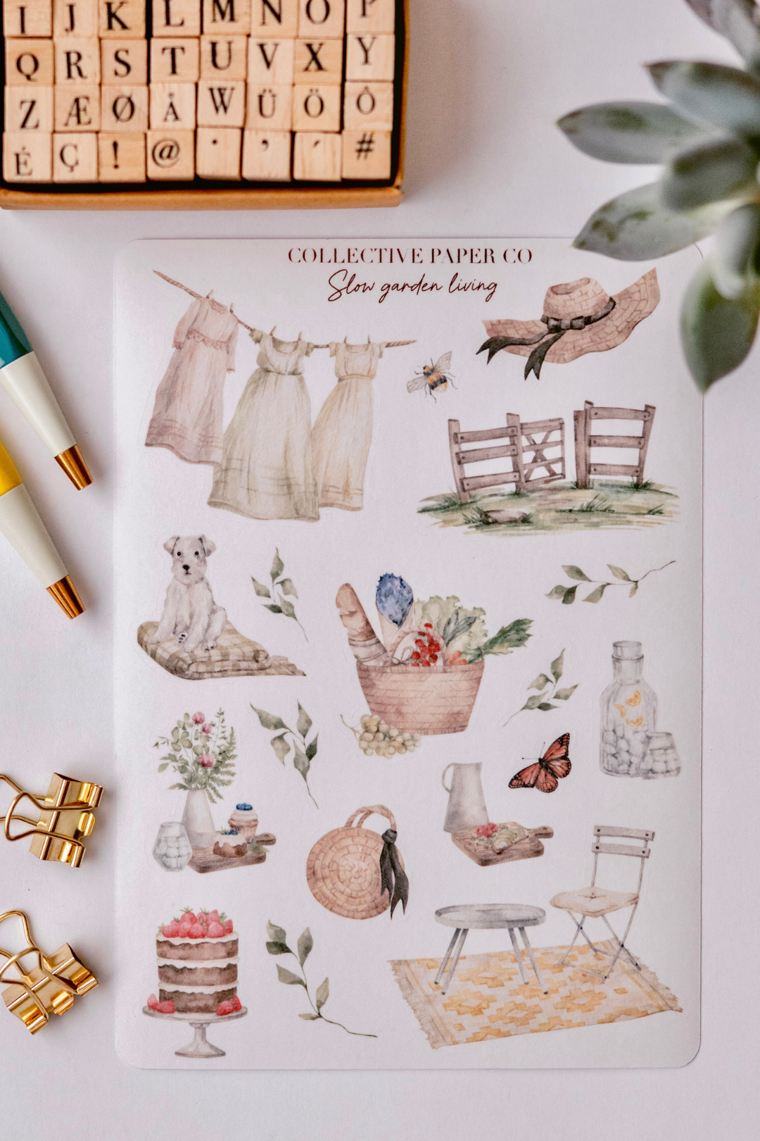 Collective Paper Co.'s Slow Garden Living washi tape shows watercolor scenes of laundry on lines, bees, fences, dogs, baskets of vegetables and grapes, butterflies, jars, teacups, cakes, chairs, and rugs.