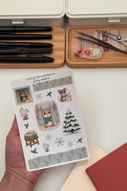 Sheet of decorative stickers featuring mice and nature elements held by a hand, with stationery items in the background.