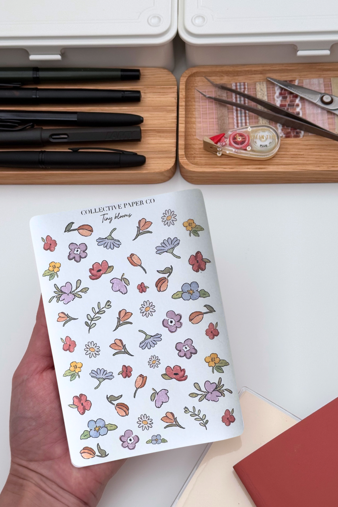 Collective Blooms Co. sticker sheet featuring scattered watercolor-style spring flowers in pink, purple, orange, and white, including tulips, daisies, and violets on a white background.