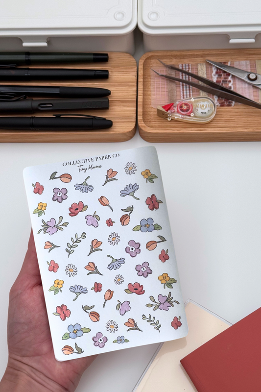 Collective Blooms Co. sticker sheet featuring scattered watercolor-style spring flowers in pink, purple, orange, and white, including tulips, daisies, and violets on a white background.