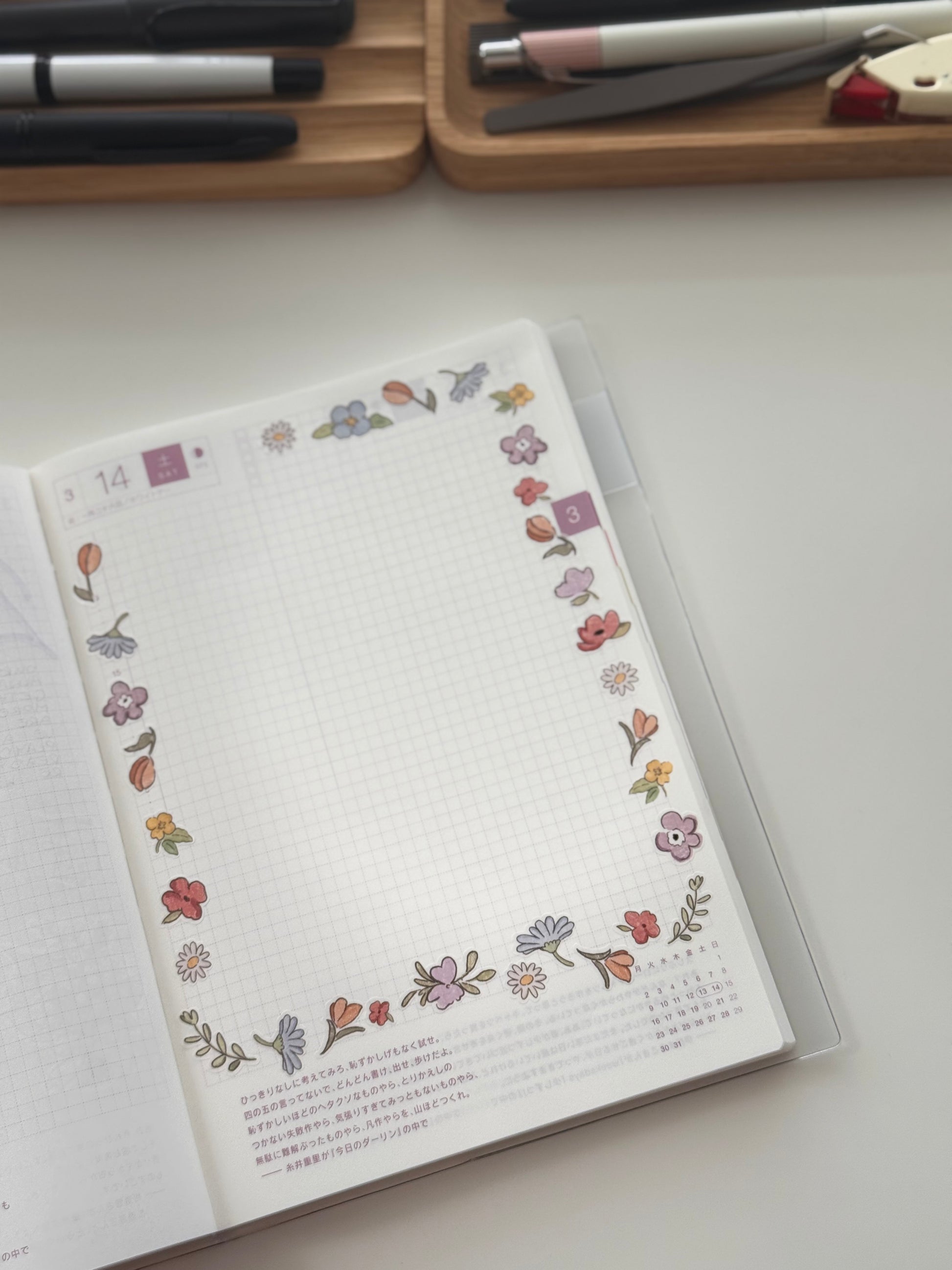 Open planner page for day 14 with blank watercolor flower border in purples, pinks, and oranges (daisies, tulips, violets) around a grid schedule and Japanese text notes.
