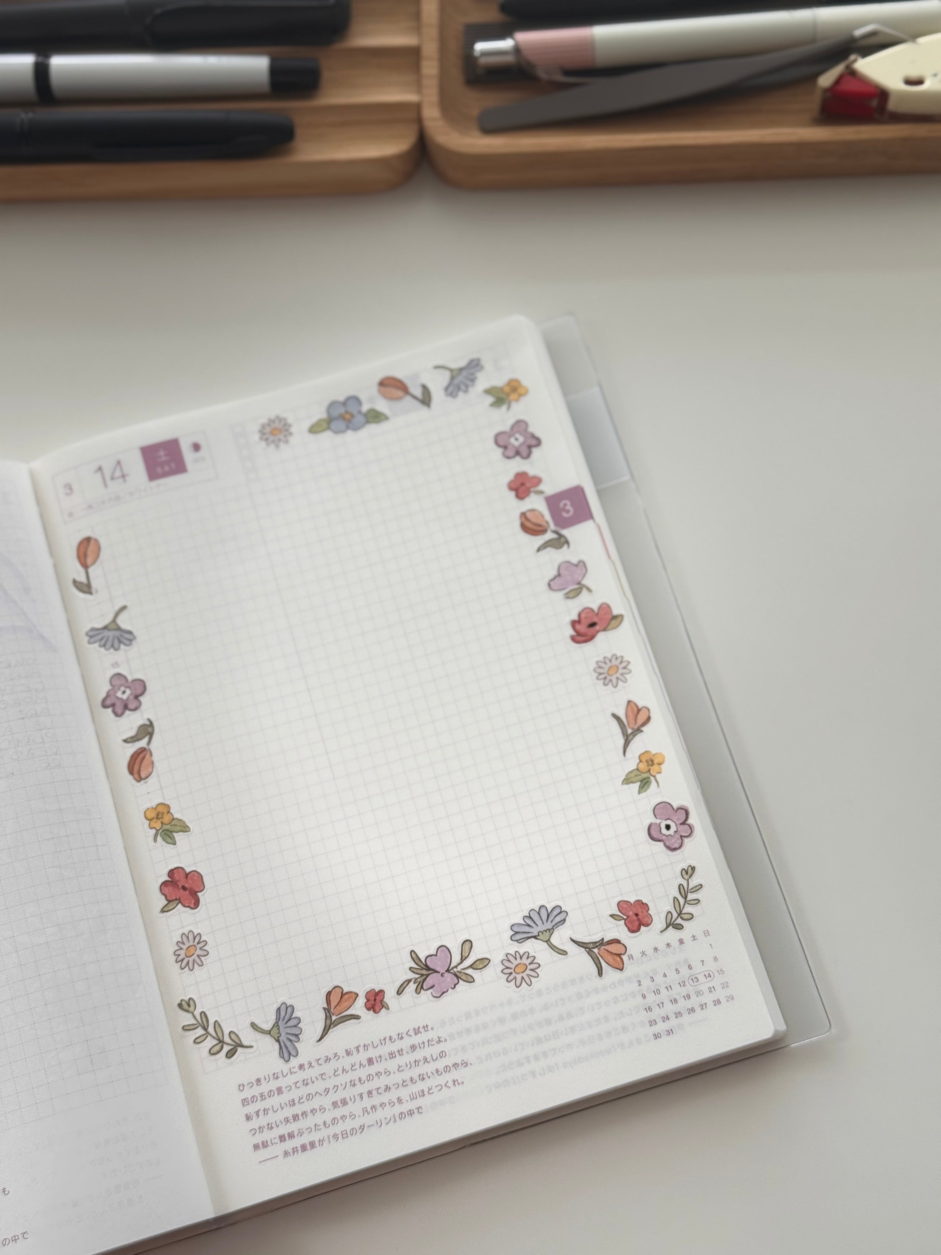 Open planner page for day 14 with blank watercolor flower border in purples, pinks, and oranges (daisies, tulips, violets) around a grid schedule and Japanese text notes.
