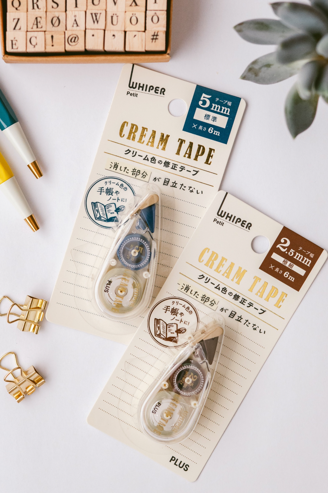 Two Whisper Pet Plus washi tape dispensers in cream color (5mm x 8m and 2.5mm x 8m) with Japanese packaging are displayed alongside a potted succulent and gold accents.