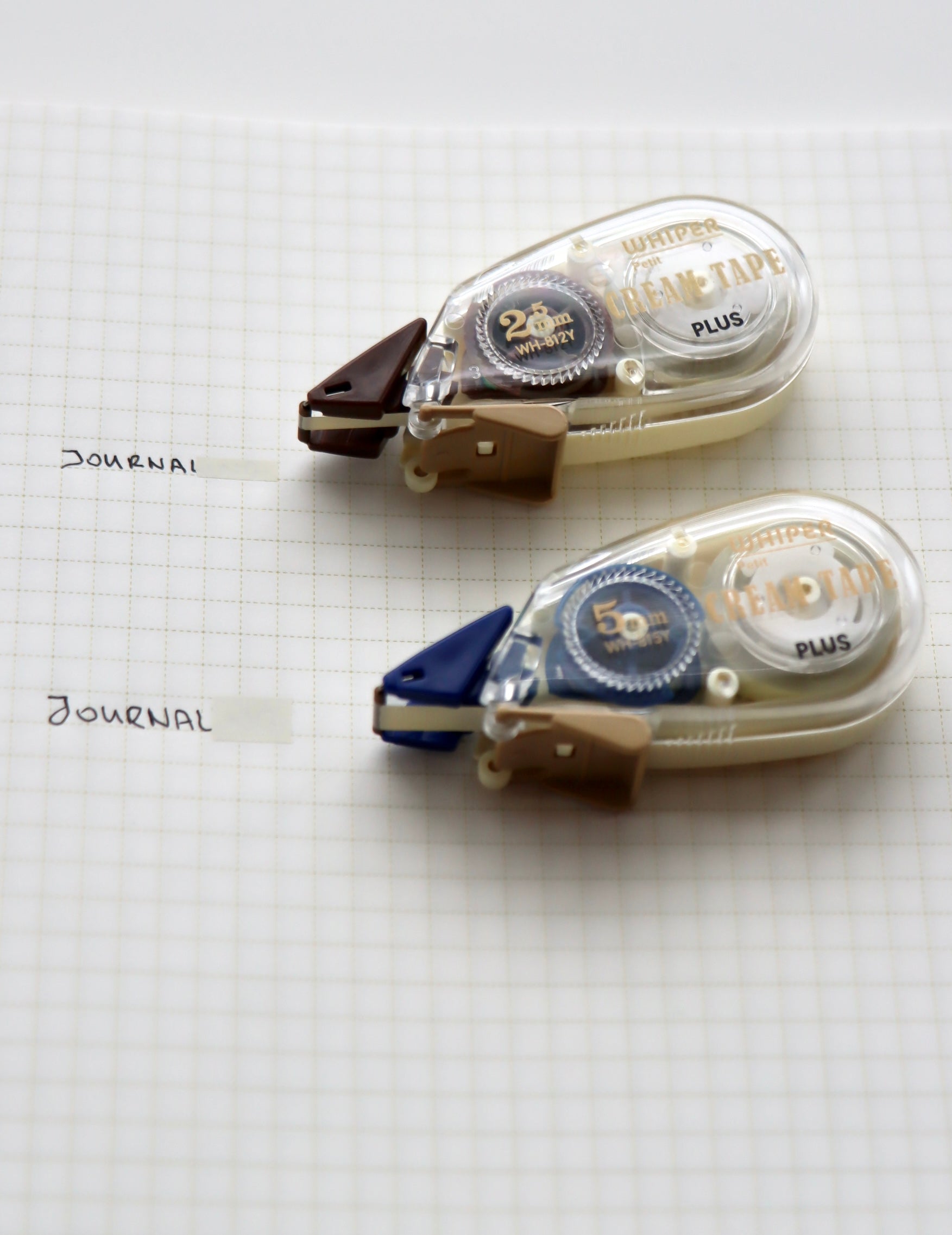 Two Whisper Chara Tape Plus dispensers—one brown for 25mm width (10m) and one blue for 50mm width (9m)—with built-in cutters, arranged on graph paper.
​

