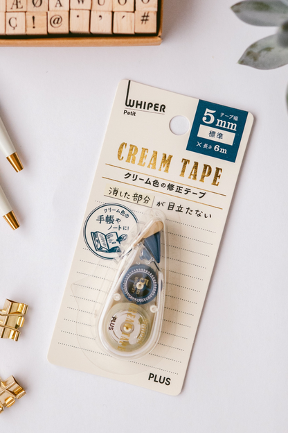 A Whisper Pet Plus washi tape dispensers in cream color (5mm x 8m and 2.5mm x 8m) with Japanese packaging are displayed alongside a potted succulent and gold accents.