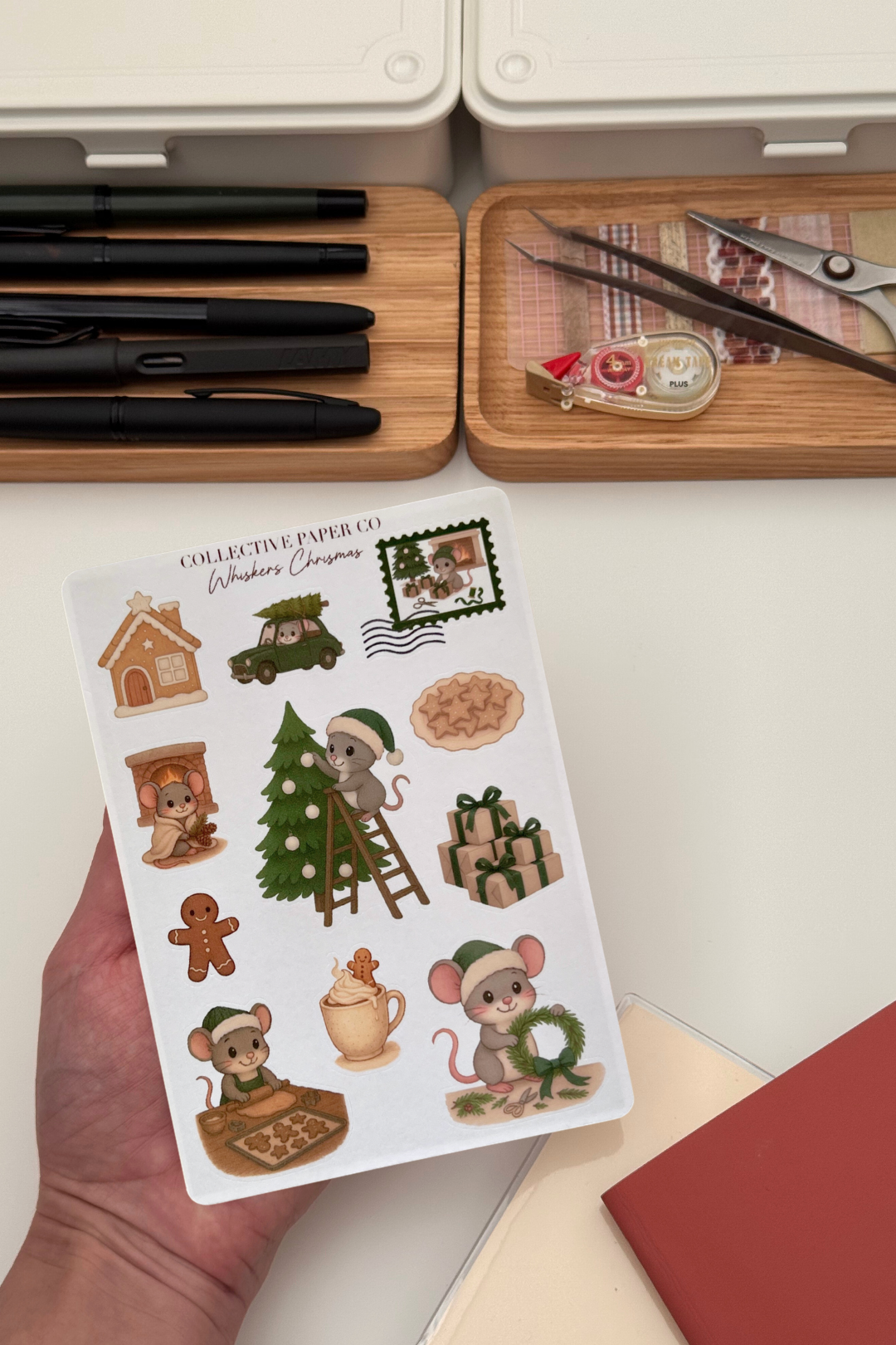 Sheet of Christmas-themed stickers held by a hand with stationery items in the background.