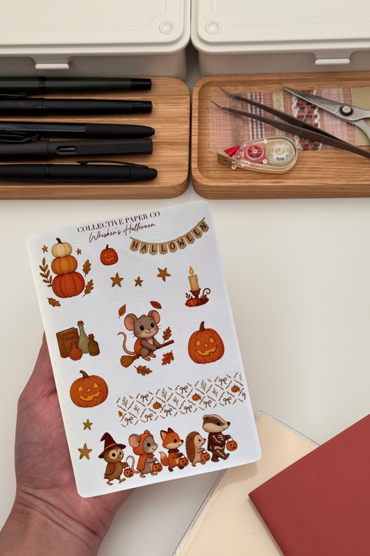 Sheet of Halloween-themed stickers held by a hand with stationery items in the background.