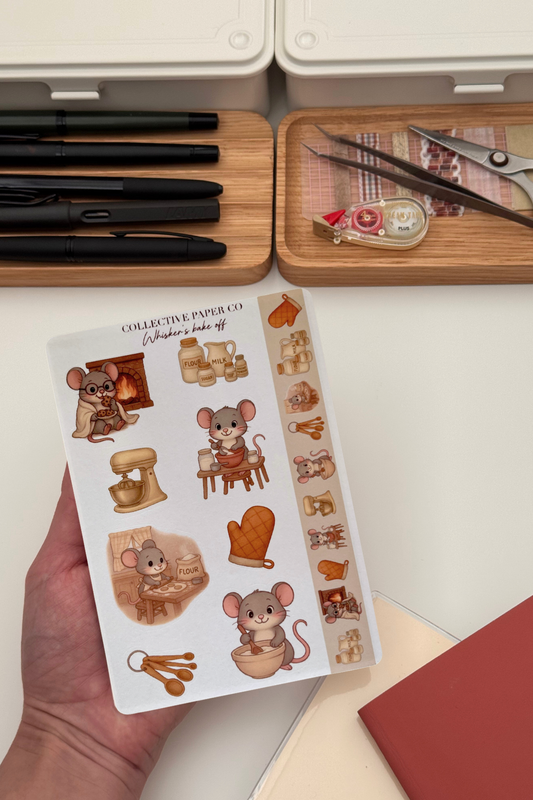 Sheet of stickers with cartoon mice and baking items held by a hand, with stationery items in the background.