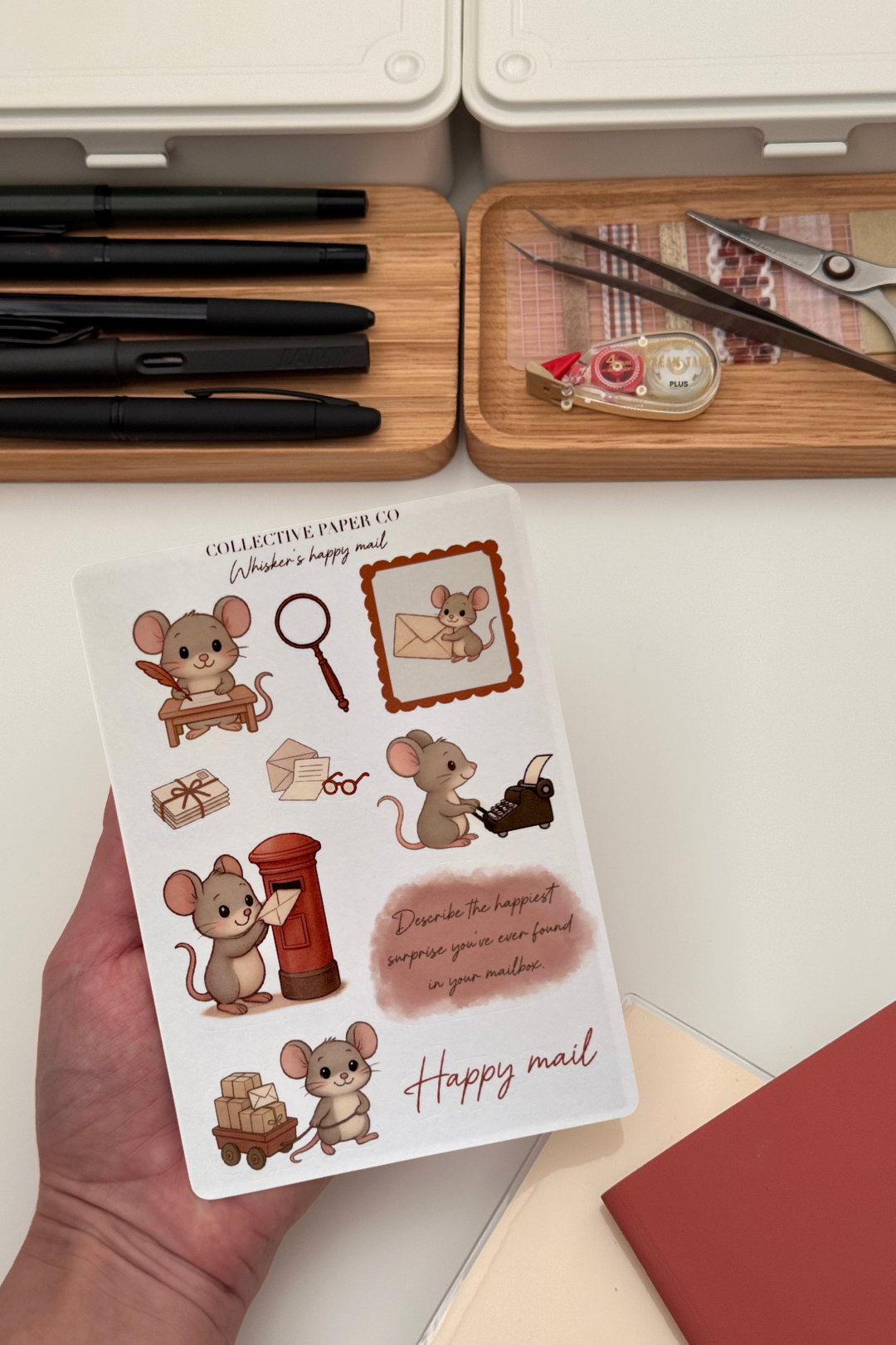 Sheet of mouse-themed stickers held by a hand with stationery items in the background.