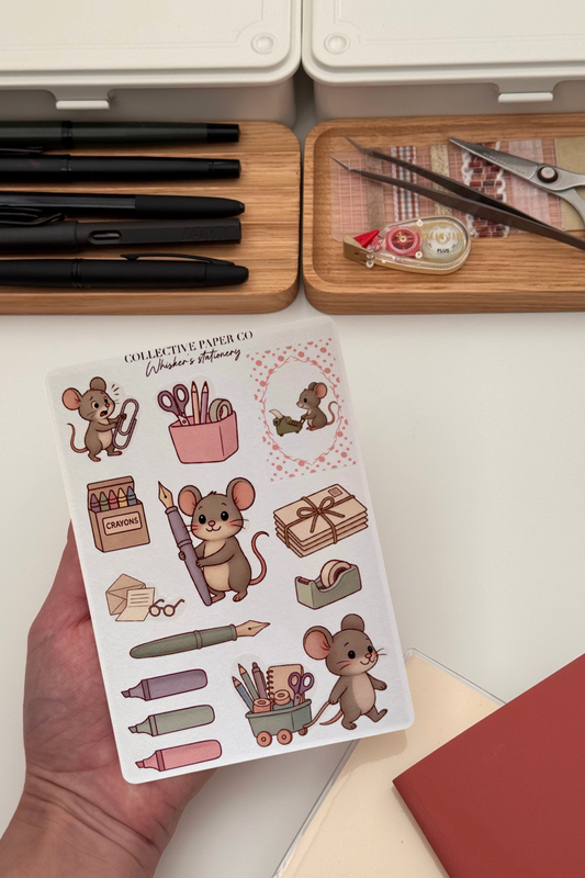 Sheet of mouse-themed stickers held by a hand with stationery items in the background.